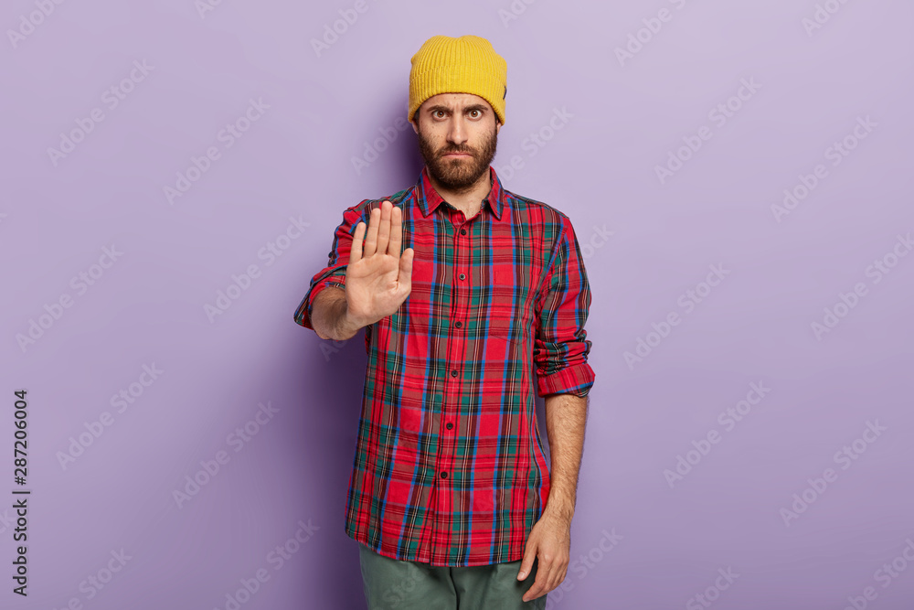 Photo of serious stern unshaven man shows stop gesture, dressed in fashionable clothes, refuses something, asks not to do forbidden actions, isolated over purple background. Body language concept Photo of serious stern unshaven man shows stop gesture, dressed in fashionable clothes, refuses something, asks not to do forbidden actions, isolated over purple background. Body language concept