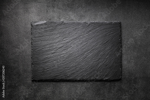 Black slate board on dark stone texture top view. Empty space for menu or recipe.