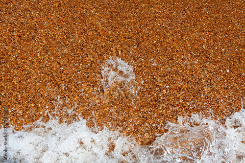 A wave rushes to the sandy shore from coarse sand.