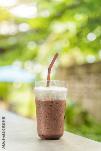 Iced chocolate topped with milk froth in a plastic cup with brown straw.