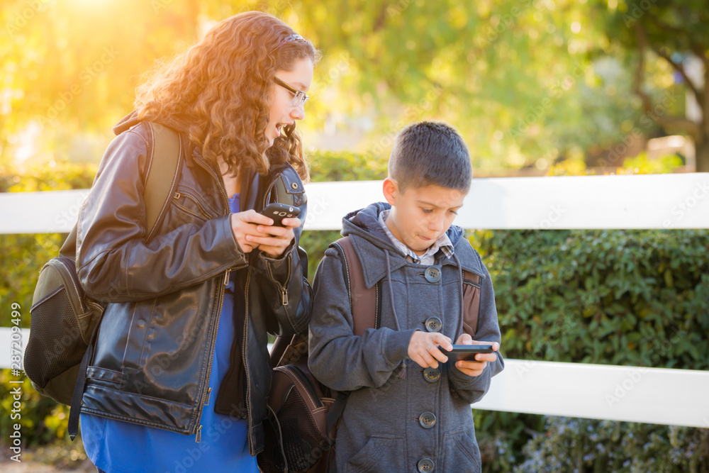 Obraz premium Hispanic Brother and Sister Wearing Backpacks Walking Texting On Cell Pones