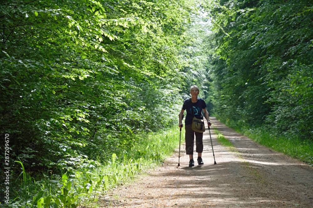 Fototapeta premium seniorin mit krücken geht auf einem waldweg