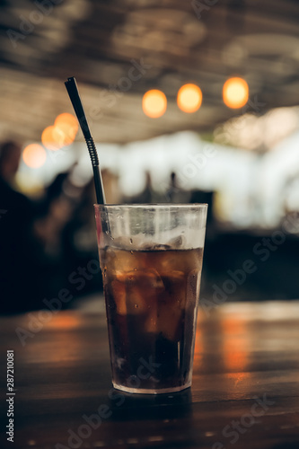glass of cola with ice on a wooden table at an outdoor summer cafe. peoples on background. vertical