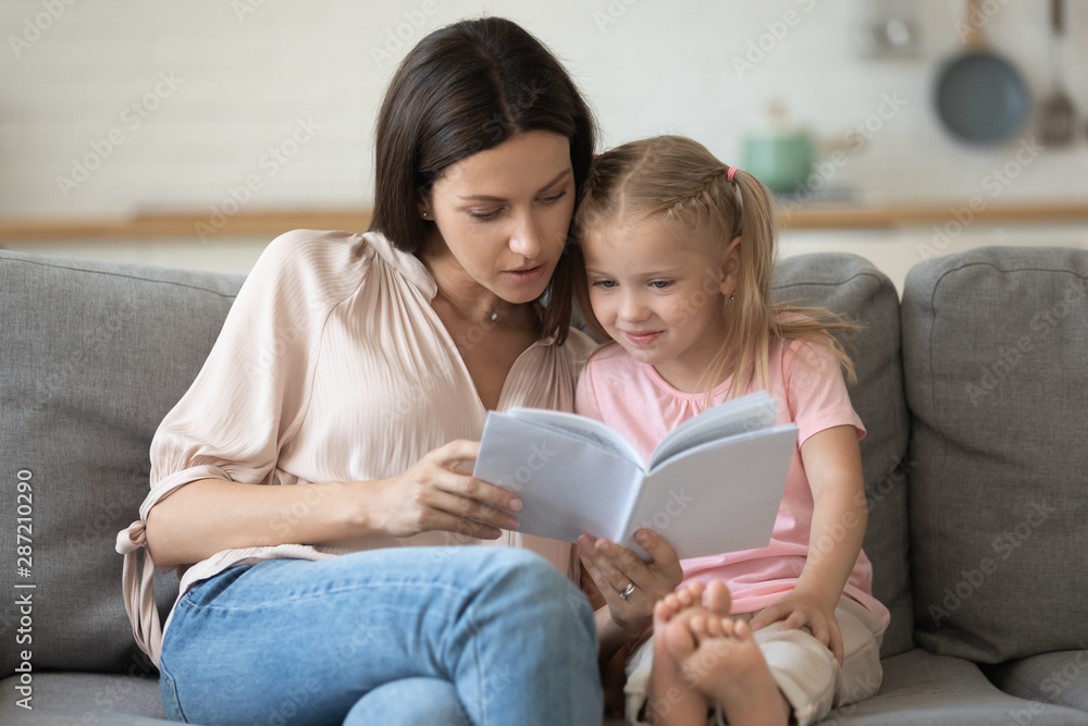 Mother and daughter sitting on couch reading a book Mother and daughter sitting on couch reading a book