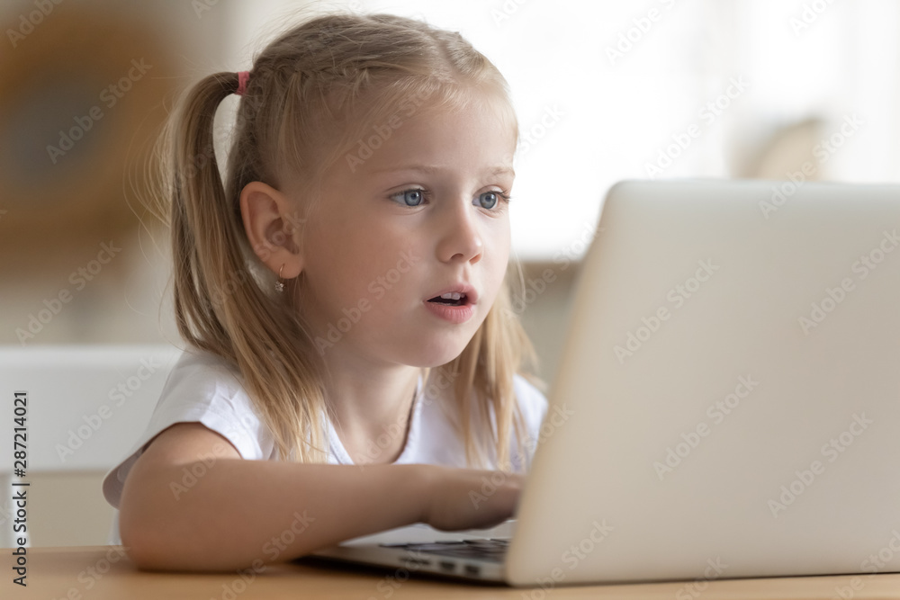 Little girl sitting at table watching cartoons on laptop