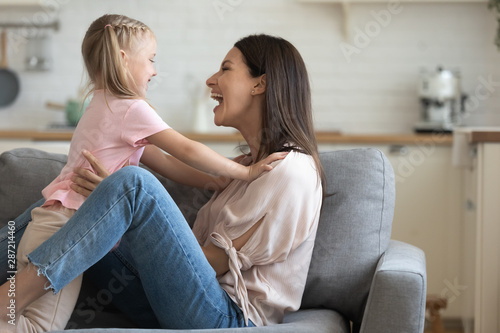 Hilarious mother holding daughter by waist having fun together indoors