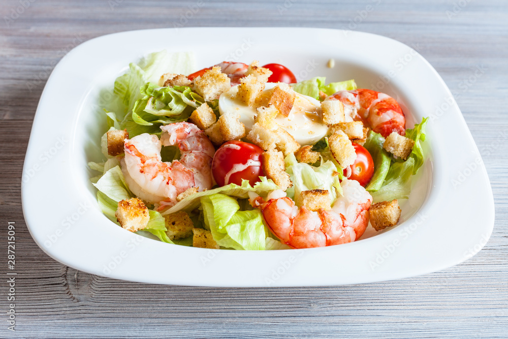 Caesar salad with prawns on white plate on table Caesar salad with prawns on white plate on table