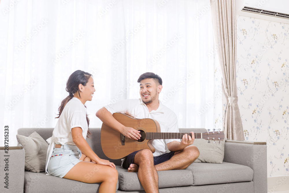 Obraz premium Handsome young asian man playing acoustic guitar and singing for his beautiful girlfriend