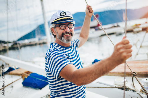 Mature man standing and laughing at helm of sailboat out at sea on a sunny afternoon.