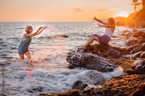 Two young beautiful girls have fun splashing in the sea at sunset.