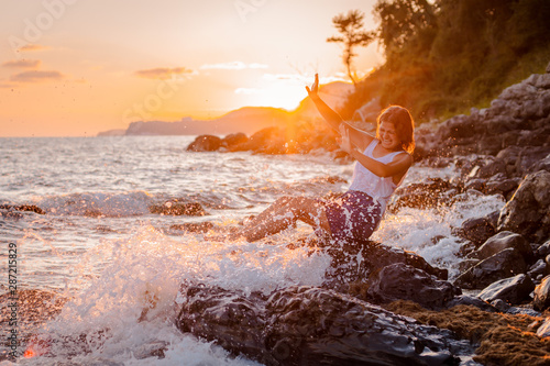 One young beautiful girl splashes and splashes the sea at sunset. Summer landscape sea, Islands and orange sunlight.