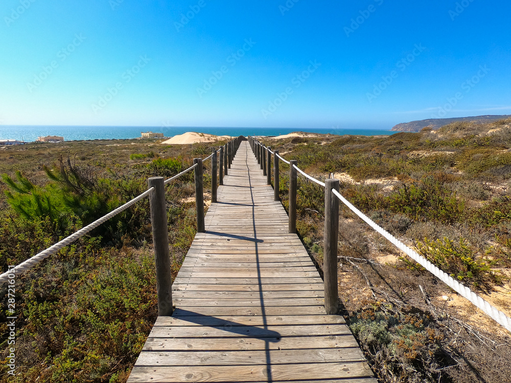Wooden footpath through dunes in the Atlantic ocean coast. Guincho beach at sunset, Cascais Portugal Wooden footpath through dunes in the Atlantic ocean coast. Guincho beach at sunset, Cascais Portugal