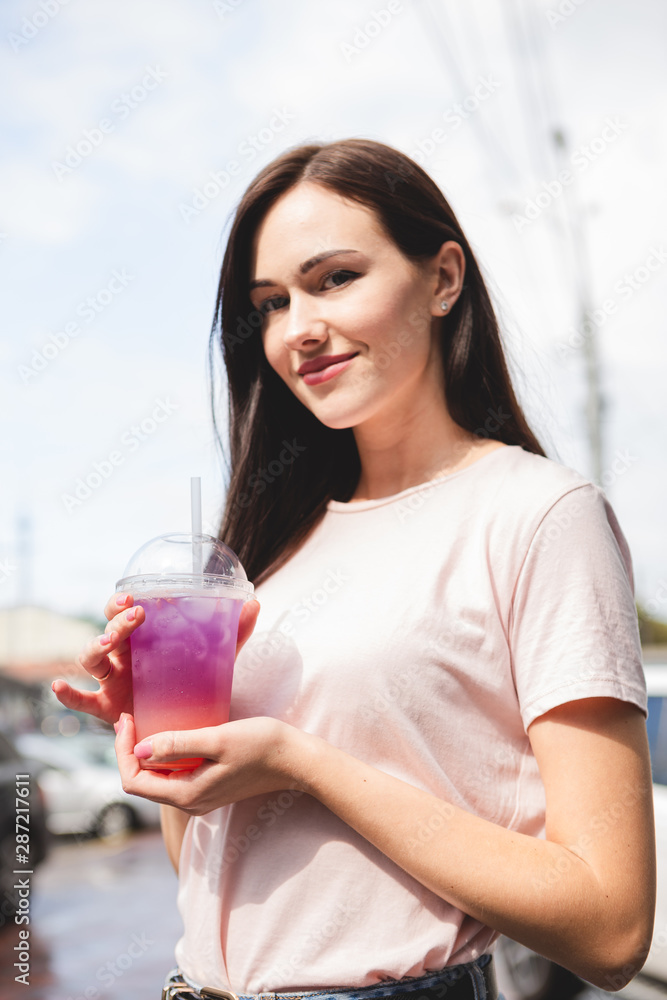 pretty and attractive woman holding a plastic glass with a cold multicolored summer cocktail with a good smile and cheerful mood pretty and attractive woman holding a plastic glass with a cold multicolored summer cocktail with a good smile and cheerful mood
