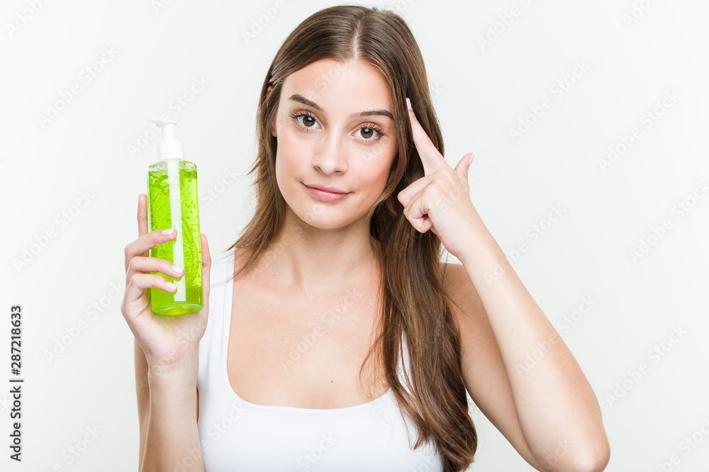 Young caucasian woman holding an aloe vera bottle pointing his temple with finger, thinking, focused on a task. Young caucasian woman holding an aloe vera bottle pointing his temple with finger, thinking, focused on a task.