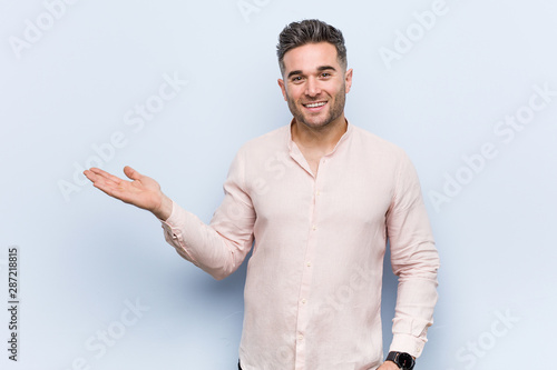 Young handsome cool man showing a copy space on a palm and holding another hand on waist.