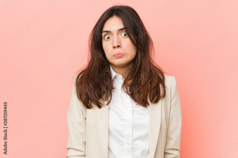 Young brunette business woman against a pink background shrugs shoulders and open eyes confused. Young brunette business woman against a pink background shrugs shoulders and open eyes confused.