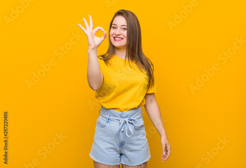 Young woman teenager wearing a yellow shirt cheerful and confident showing ok gesture.