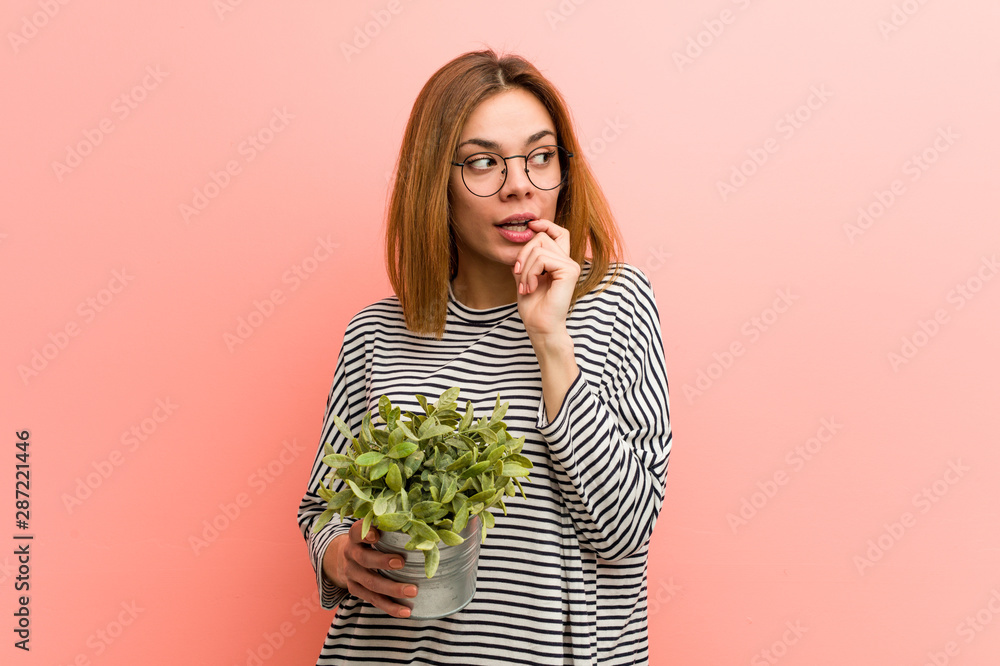 Young woman holding a plant relaxed thinking about something looking at a copy space. - obrazy, fototapety, plakaty 