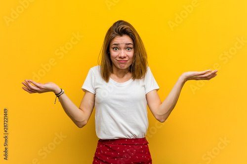 Young natural caucasian woman doubting and shrugging her shoulders in questioning gesture.