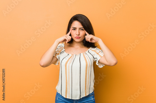 Young curvy woman focused on a task, keeping forefingers pointing head.