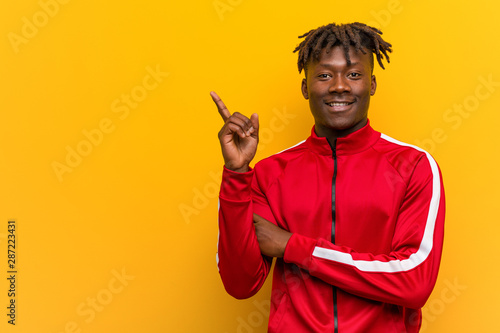 Young fitness african man smiling cheerfully pointing with forefinger away.
