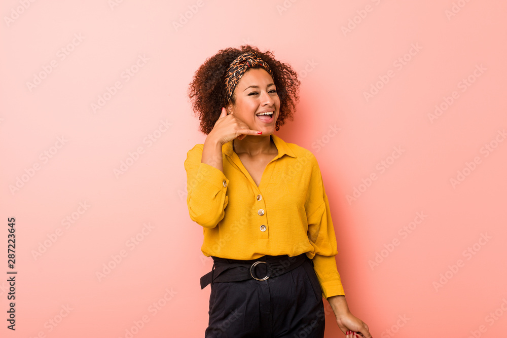 Young african american woman against a pink background showing a mobile phone call gesture with fingers. Young african american woman against a pink background showing a mobile phone call gesture with fingers.