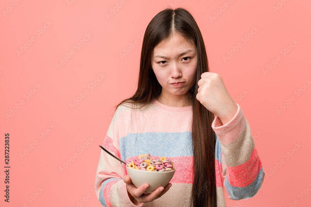 Young asian woman with a cereal bowl showing fist to camera, aggressive facial expression. Young asian woman with a cereal bowl showing fist to camera, aggressive facial expression.
