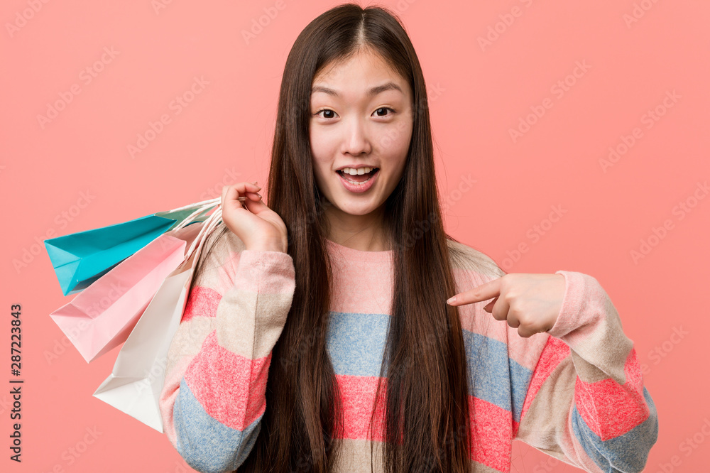 Young asian woman holding a shopping bag surprised pointing at himself, smiling broadly. Young asian woman holding a shopping bag surprised pointing at himself, smiling broadly.