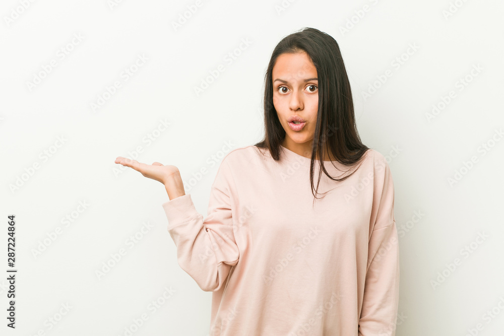 Young cute hispanic teenager woman impressed holding copy space on palm. Young cute hispanic teenager woman impressed holding copy space on palm.