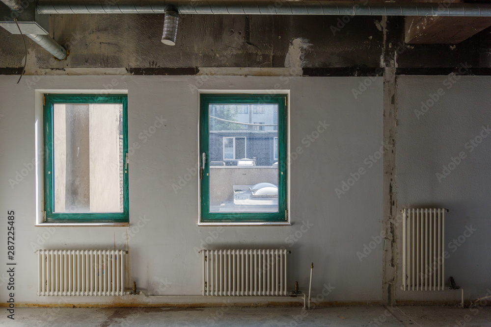 Interior view of empty abandon room with radiator heaters, glass windows and air duct system on ceiling.