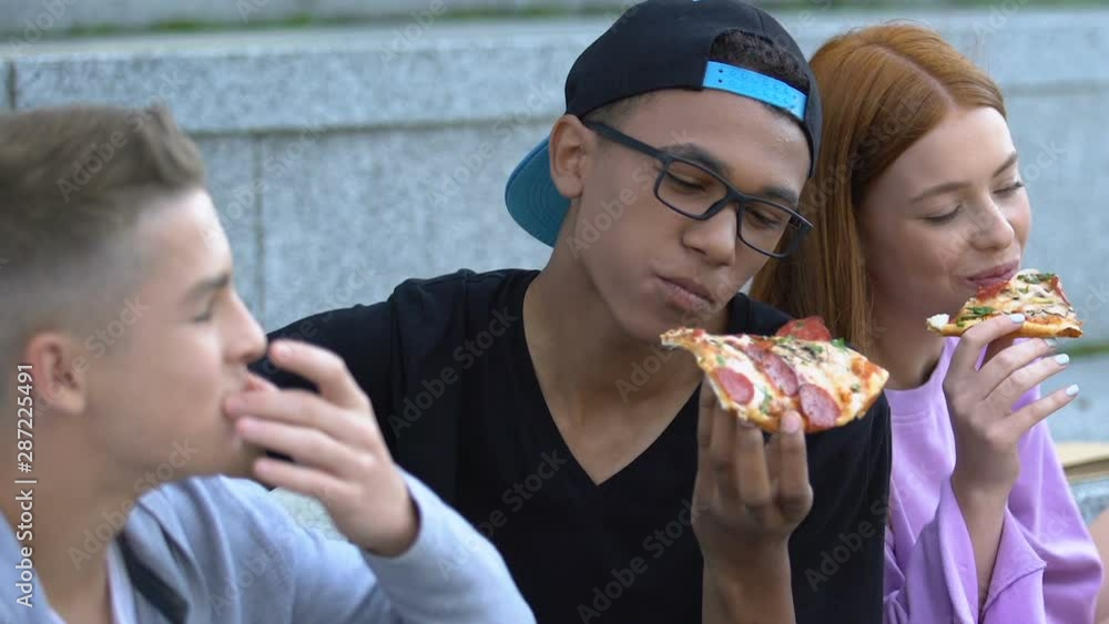 Satisfied multiracial male friends and girl eating delicious pizza and laughing Satisfied multiracial male friends and girl eating delicious pizza and laughing