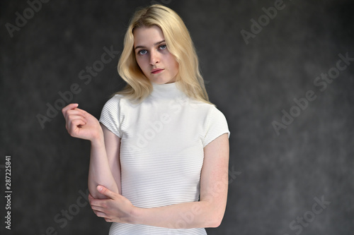 Portrait of a cute blonde girl, a young woman in a white sweater with beautiful curly hair on a gray background. Shows hands to the sides. Beauty, brightness, emotions.