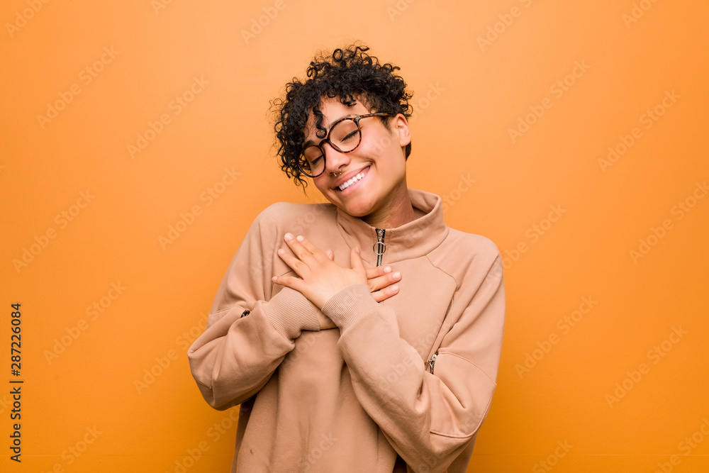 Fototapeta premium Young mixed african american woman against a brown background has friendly expression, pressing palm to chest. Love concept.