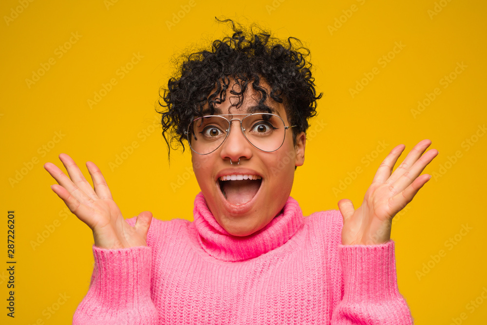 Young african american woman wearing a pink sweater celebrating a victory or success, he is surprised and shocked. Young african american woman wearing a pink sweater celebrating a victory or success, he is surprised and shocked.
