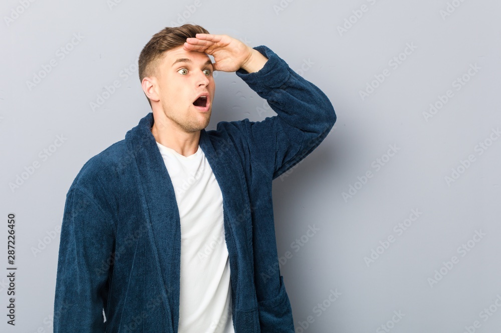 Young caucasian man wearing pajama looking far away keeping hand on forehead. Young caucasian man wearing pajama looking far away keeping hand on forehead.
