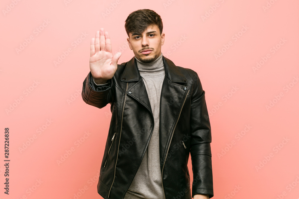 Young hispanic man wearing a leather jacket standing with outstretched hand showing stop sign, preventing you. Young hispanic man wearing a leather jacket standing with outstretched hand showing stop sign, preventing you.