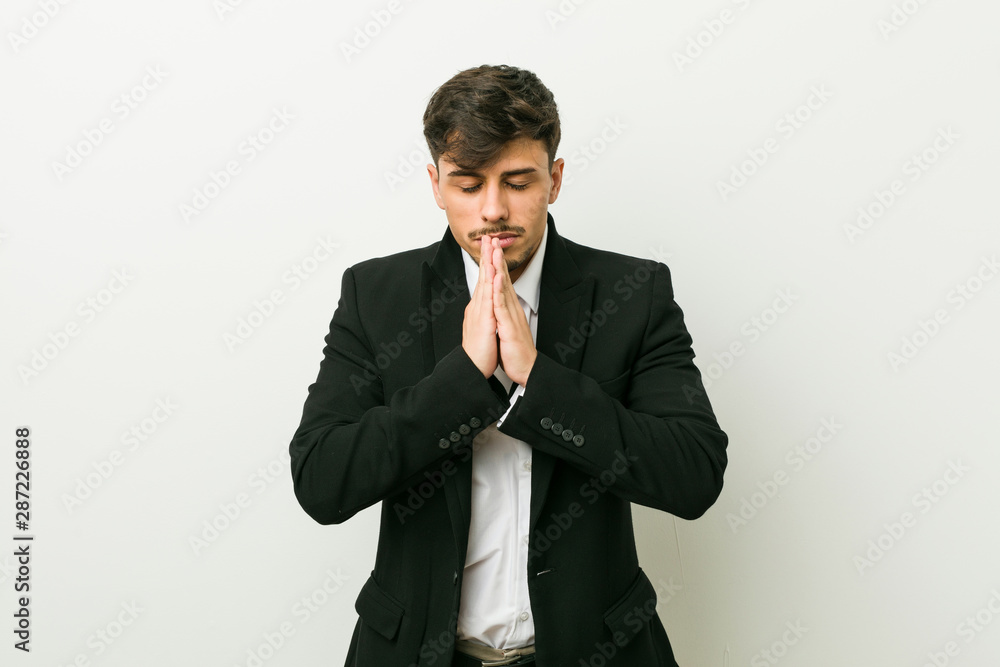 Young business hispanic man holding hands in pray near mouth, feels confident. Young business hispanic man holding hands in pray near mouth, feels confident.