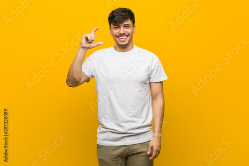Young hispanic casual man holding something little with forefingers  smiling and confident.
