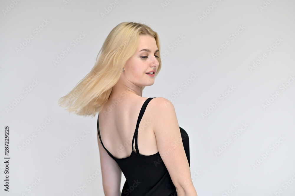 Portrait of a cute blonde student girl, a young woman in a black dress with beautiful curly hair on a white background in different poses. Shows hands to the sides. Beauty, brightness, emotions. Portrait of a cute blonde student girl, a young woman in a black dress with beautiful curly hair on a white background in different poses. Shows hands to the sides. Beauty, brightness, emotions.