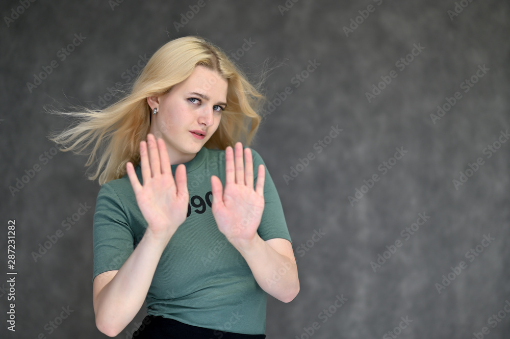 Portrait of a cute blonde student girl, a young woman in a green T-shirt with beautiful curly hair on a gray background in different poses. Shows hands to the sides. Beauty, brightness, emotions. Portrait of a cute blonde student girl, a young woman in a green T-shirt with beautiful curly hair on a gray background in different poses. Shows hands to the sides. Beauty, brightness, emotions.