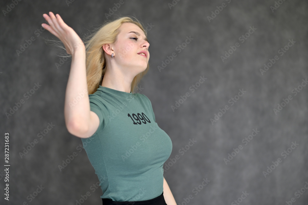Portrait of a cute blonde student girl, a young woman in a green T-shirt with beautiful curly hair on a gray background in different poses. Shows hands to the sides. Beauty, brightness, emotions. Portrait of a cute blonde student girl, a young woman in a green T-shirt with beautiful curly hair on a gray background in different poses. Shows hands to the sides. Beauty, brightness, emotions.