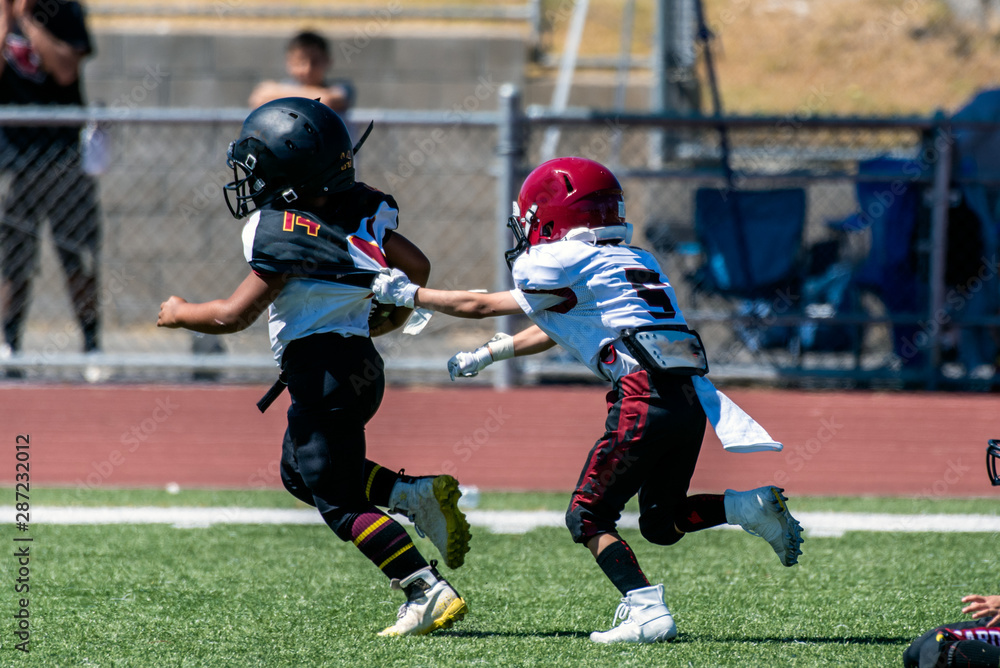 Break away play on youth football game has defensive player grasping the jersey of the escaping offensive athlete. Break away play on youth football game has defensive player grasping the jersey of the escaping offensive athlete.