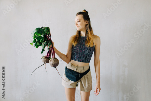 young pretty girl holding fresh organic beet on grey background