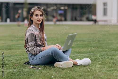 Woman sitting on green grass in park during summer day while using laptop