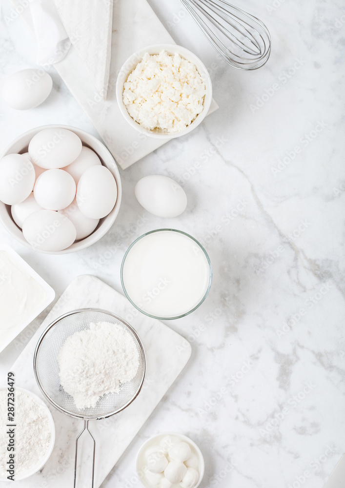 Fresh dairy products on white marble background. Glass of milk, bowl of flour, sour cream and cottage cheese and eggs. Steel whisk. Top view. Fresh dairy products on white marble background. Glass of milk, bowl of flour, sour cream and cottage cheese and eggs. Steel whisk. Top view.