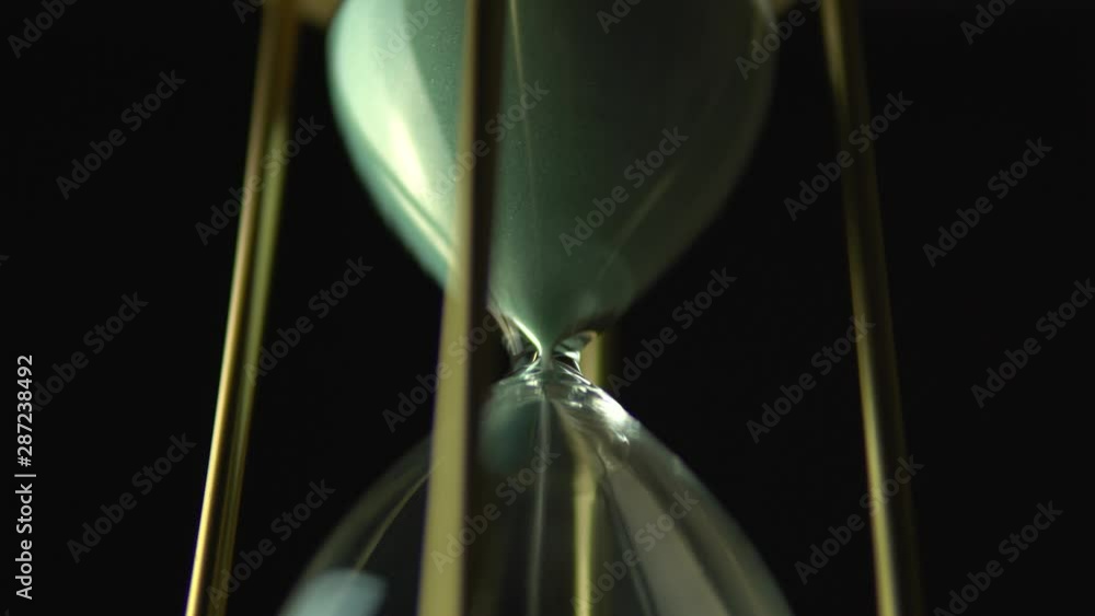Slow motion rotation of sand timer clock with sand flowing from through