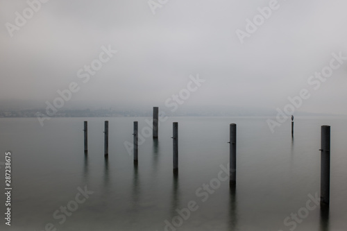 Zürichsee mit Nebel im Herbst mit Pfeilern einer Anlagestelle für Schiffe