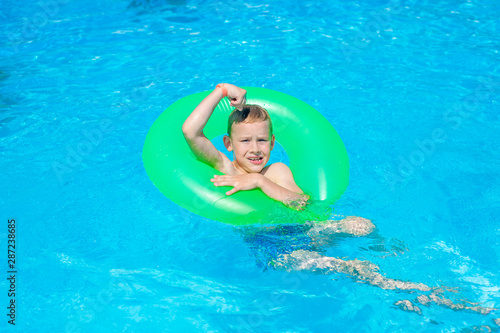 Happy kid boy having fun in an swimming pool. Active happy healthy preschool child learning to swim. With safe floaties or swimmies.