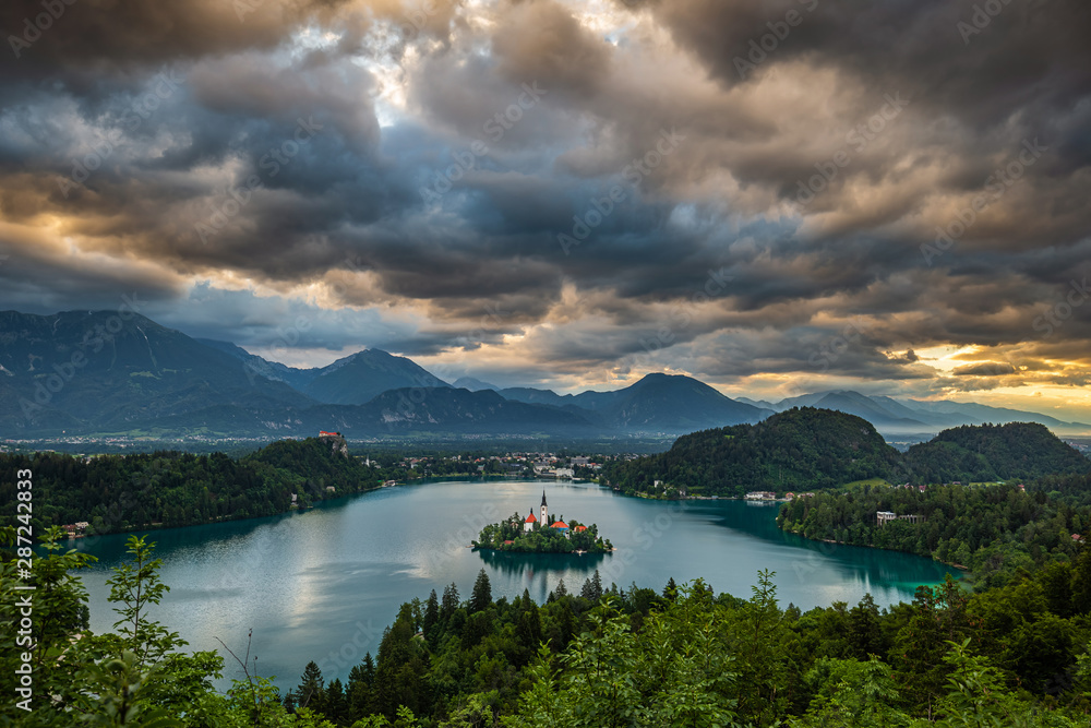 Bled, Slovenia - Dramatic sky and clouds above Lake Bled (Blejsko Jezero) with the Pilgrimage Church of the Assumption of Maria on an island and Julian Alps at background on a beautiful summer morning