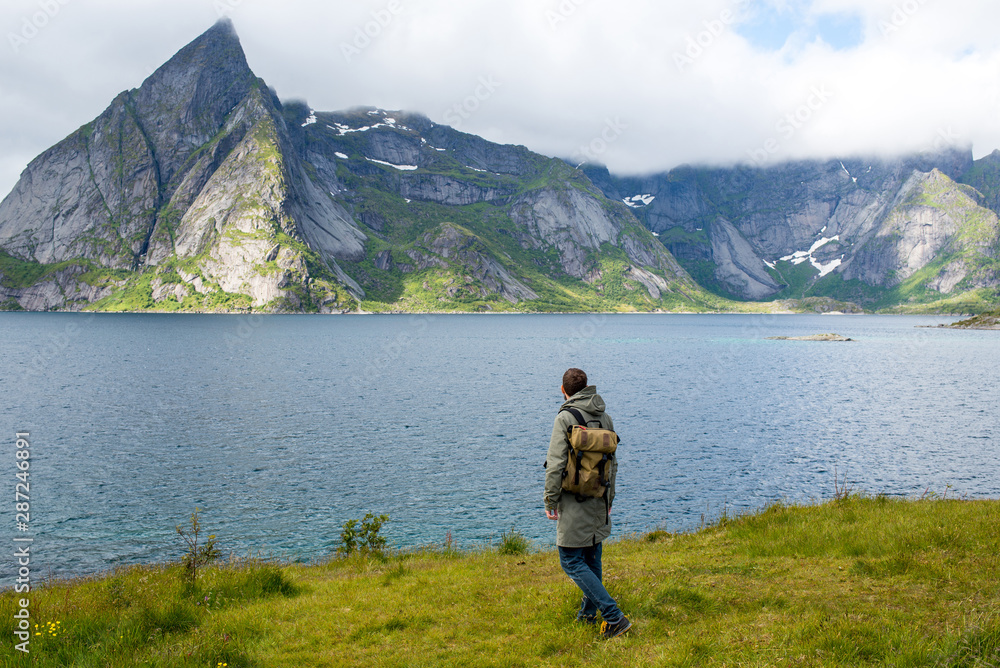 A man with a backpack looks at the fjord. Beautiful nature landscape in North. Amazing scenic outdoor view. Enjoy the moment, relaxation. Wanderlust. Travel, adventure, lifestyle. Explore Norway